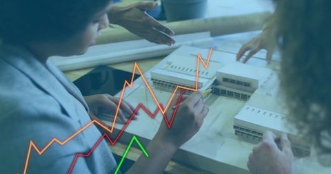 Diverse Business Team Working on Architectural Model with Financial Data Overlay