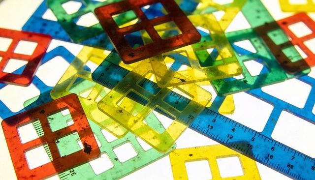 Stacking colorful translucent square stencils over backlit grid with blue ruler and scratches