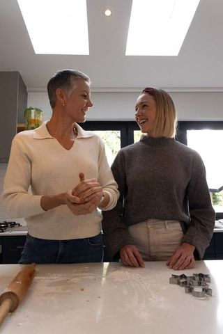 Senior and midlife women baking cookies together in modern sunlit kitchen