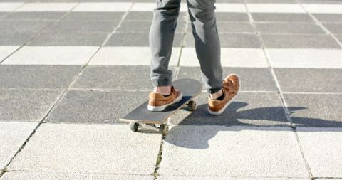 Male balancing on skateboard on urban checkerboard plaza wearing brown sneakers
