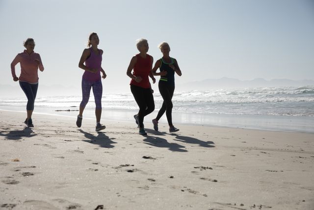 Group of Caucasian female friends running on the beach on a sunny day, enjoying exercise and smiling. Ideal for promoting active lifestyles, fitness, wellness, and outdoor activities. Suitable for use in health and fitness campaigns, travel brochures, and social media posts about friendship and healthy living.