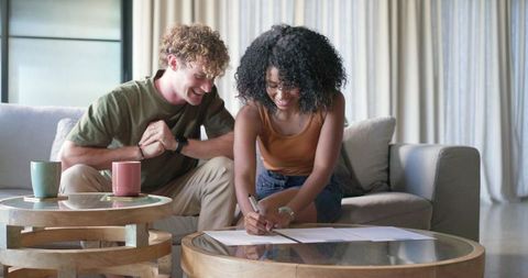 Diverse couple signing rental agreement on living room table, smiling and relaxed