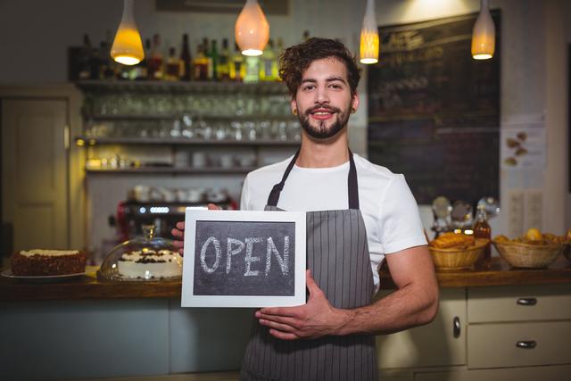 Portrait of smiling waiter showing slate with open sign in cafÃ©