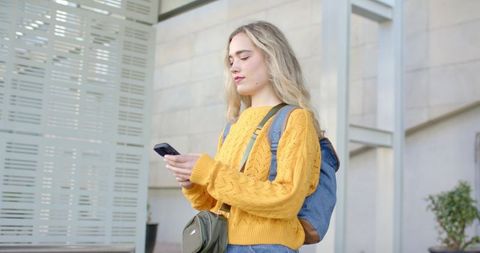 Young woman checking phone while standing at modern architectural building entrance
