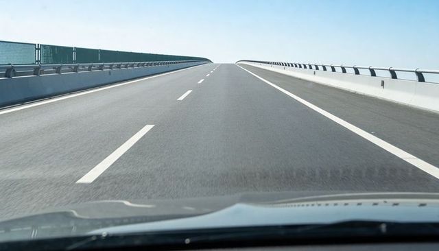 Driver view on elevated highway rising toward horizon under clear blue sky