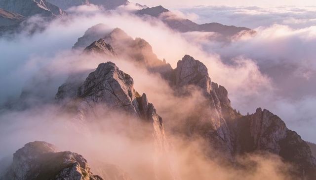 Ridge of jagged alpine peaks piercing glowing mist at sunrise, dramatic mountain panorama