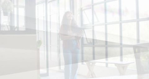 Smiling woman holding tablet, gazing upward in bright minimalist loft with grid windows