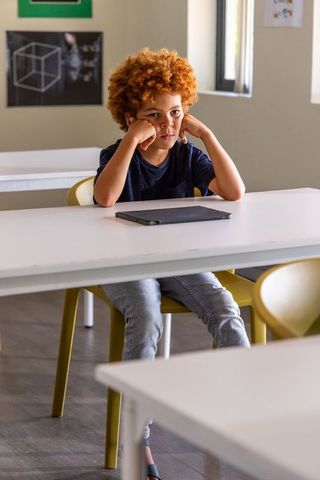 Pensive african american school boy sitting at desk with closed tablet reflecting screen fatigue