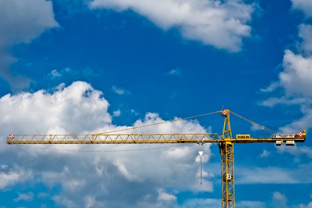 Yellow construction crane extending against a vibrant blue sky filled with fluffy white clouds. Ideal for use in topics related to construction, urban development, architecture, engineering, and industrial equipment. Can also highlight themes of growth, progress, and modernization in both online and printed media.