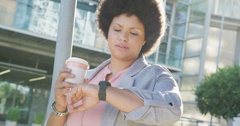 Confident businesswoman checks smartwatch while enjoying coffee outdoors