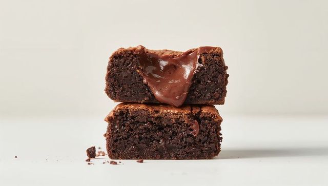 Fudgy brownies oozing glossy chocolate ganache stacked on white tabletop, crumb detail