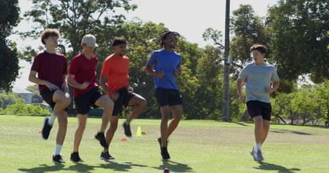 Five male athletes performing high-knee drill on grass during outdoor team agility training