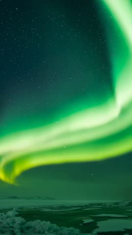 Vertical aurora borealis sweeping over frozen coastline night sky with star field
