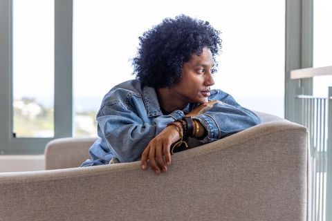 African american woman leaning over sofa gazing at ocean from bright coastal apartment