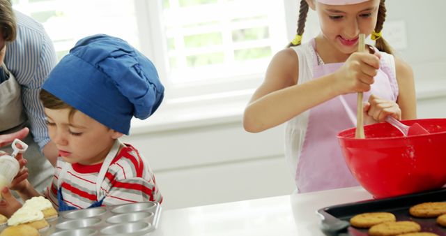 Children enjoying a baking session in a bright modern kitchen. Girl is mixing ingredients in a red bowl, and boy is preparing cupcakes. This image is ideal for promoting family bonding activities, cooking classes for children, educational programs, or kitchen products. Perfect visual for blogs, articles, or advertising materials focused on kid-friendly recipes, family fun, and culinary education.