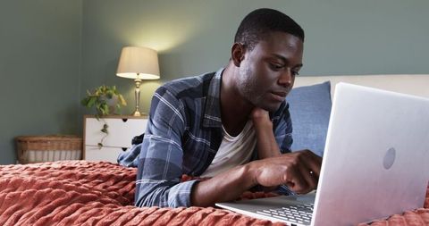 Man working from bed using laptop in cozy home setting
