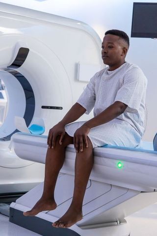 Male patient sitting on ct scanner table in hospital gown awaiting diagnostic scan