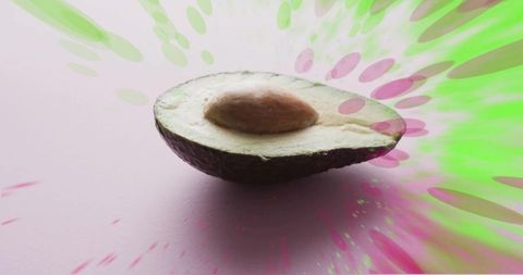 Halved avocado showing pit on pastel pink with neon green and pink burst