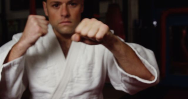Martial artist standing with fists raised, demonstrating combat readiness in a dojo. Ideal for use in materials related to martial arts training, self-defense classes, fitness motivation, and discipline-focused content.
