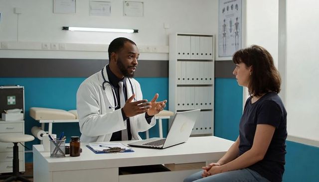 Physician consulting patient at clinic desk using laptop and explaining treatment options