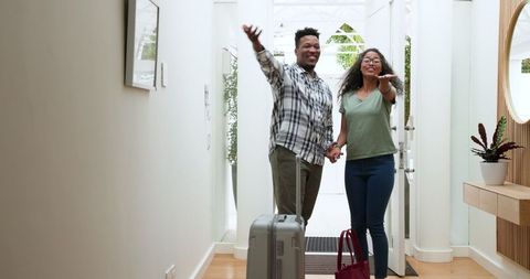 Happy Couple Arriving Home with Suitcase Holding Hands