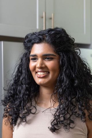 Indian woman smiling and looking left in kitchen, curly hair closeup, sleeveless beige top