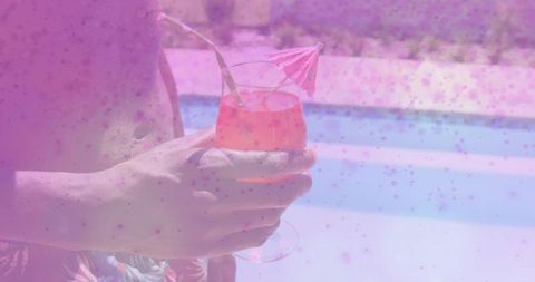 Holding man in sarong offering pink orange cocktail paper umbrella poolside summer resort