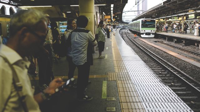 This scene captures daily life in a busy Japanese train station with commuters waiting for an arriving train. It is ideal for depicting urban transportation, travel newsletters, blogs on Japan, public transit systems, and busy city lifestyles.