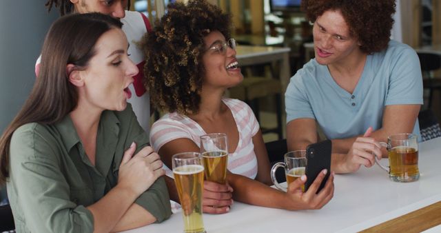 Diverse group of happy friends drinking beers and using smartphone at a bar. leisure time out socialising.