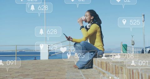 a young biracial woman sits outdoors, engaging on her smartphone surrounded by digital social media icons depicting interaction metrics like likes, comments, and shares. the image perfectly captures an engaging lifestyle emphasize tailored content for platforms looking to showcase social media usage, digital communication trends, and youth culture connectivity. this versatile image might also be useful in promoting mobile services, data plans, or apps encouraging online social participation.
