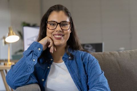 Smiling woman wearing tortoiseshell glasses relaxing on couch in modern cozy home office