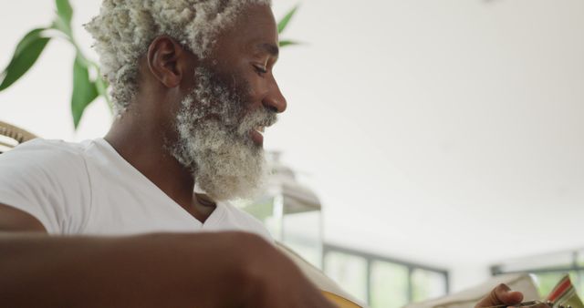 Image of sad african american senior man playing the guitar. retirement lifestyle, spending time alone at home concept digitally generated image.