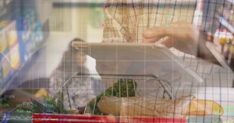 Man using tablet while grocery shopping with cart, baguette and stock market data overlay