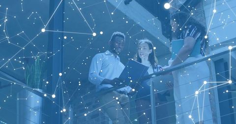 Team reviewing documents on mezzanine with digital network overlay in industrial atrium