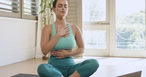 Woman meditating at home in teal sportswear finding serenity and focus
