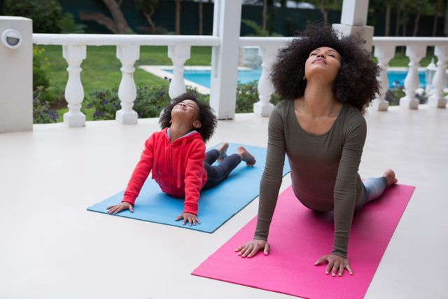 Mother and daughter practicing yoga together on porch at home. Ideal for promoting family fitness, healthy lifestyle, and bonding activities. Suitable for use in wellness blogs, fitness programs, and family-oriented advertisements.