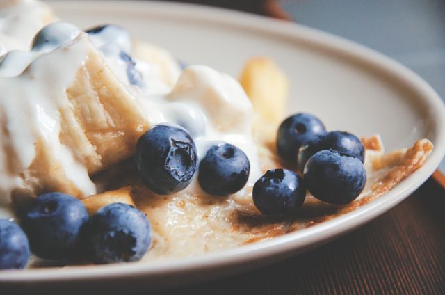 Close-up view of fresh blueberries and whipped cream on top of pancakes. Perfect for use in food blogs, recipe websites, or food packaging designs. Attractive for promoting delicious and nutritious breakfast or dessert options.