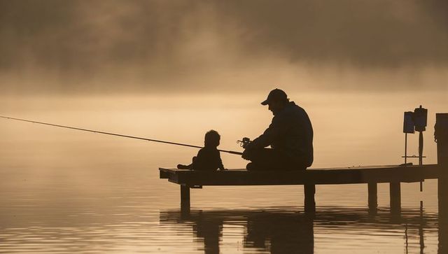 Parent and child fishing at dawn misty silhouette
