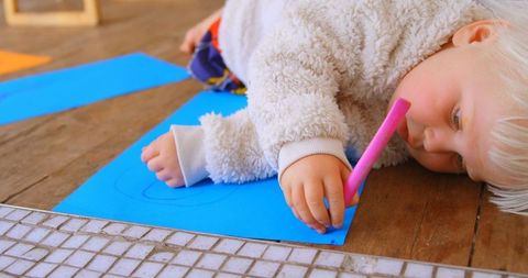 Young girl drawing on blue paper using marker indoors