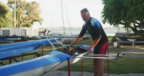 Senior man prepping rowing boat outdoors at lakeside
