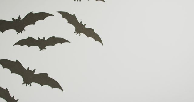 Black paper bats flying on white background create spooky atmosphere. Perfect for Halloween decoration, party decor, holiday cards, and festive promotion.