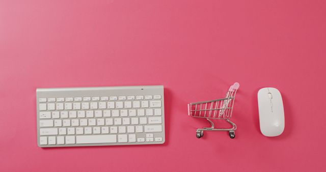 Overhead view of computer keyboard, shopping trolley and mouse on pink background with copy space. Global business, online shopping, cyber monday, sale and retail concept digitally generated image.