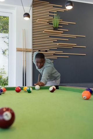 African american teenager aiming cue on pool table in modern game room