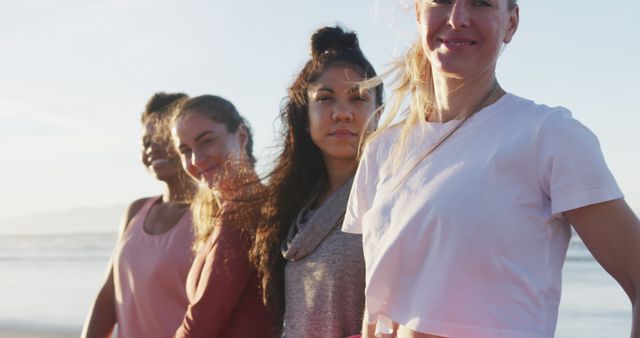 Group of women standing shoulder to shoulder on a beach with the sun setting over the ocean. They are casually dressed and smiling, fostering a sense of unity and friendship. This versatile image is ideal for concepts related to diversity, friendship, well-being, and outdoor activities.