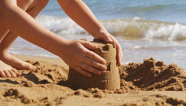 Child building sandcastle on wet shoreline closeup of hands and bare feet summer beach play
