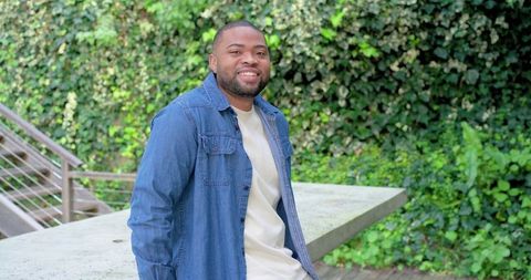 Smiling African American man leaning on patio ledge in denim shirt relaxed outdoor scene