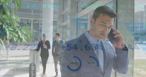 Businessman Talking on Phone Walking Through Glass Lobby with Financial Charts Overlays