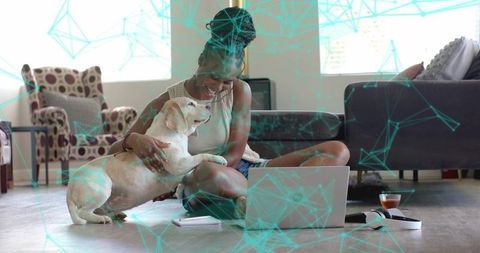 Smiling woman working from home cuddling labrador on cozy living room floor with laptop