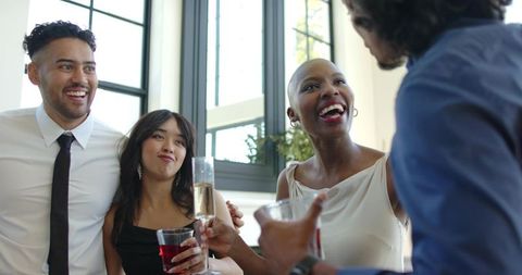 Laughing diverse friends enjoying cocktail reception in modern sunlit interior