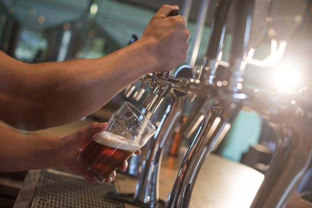 Cropped hands of bartender pouring beer from tap at bar